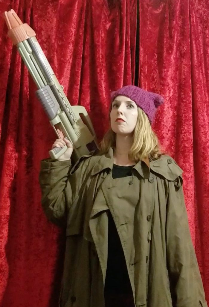20/20 Play Character Anna in a trenchcoat wearing a pussy hat and carrying a rocket launcher